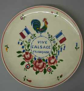 5.Manufacture de Sarreguemines, d'après Jean-Jacques Waltz dit Hansi (Colmar, 1873 ; Colmar, 1951), Plat décoratif portant l'inscription "Vive l'Alsace française", vers 1922, faïence fine, legs Mme Joseph Plfeger, 1978